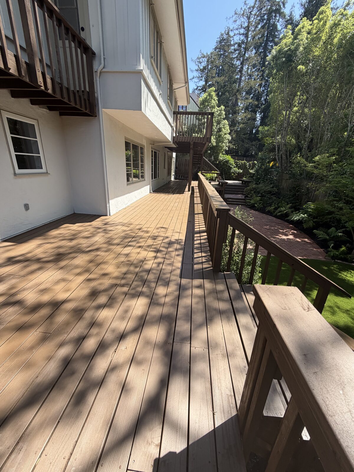 Long wood deck with railing along a hillside home