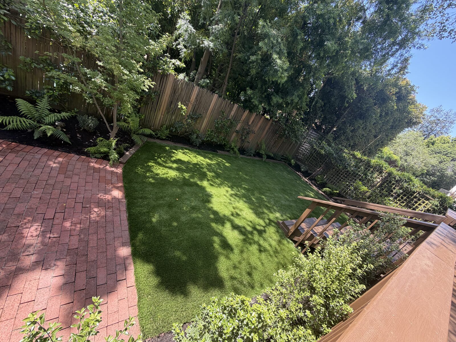 Backyard with fresh artificial turf and brick patio
